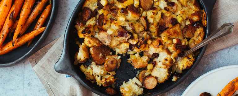 Black baking dish with stuffing next to a white dish of glazed carrots