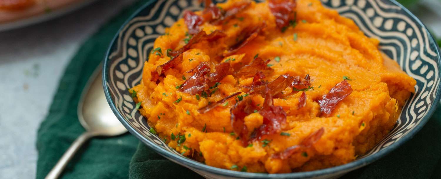 Bowl of Mashed Sweet Potatoes with Maple Prosciutto with a spoon on the side