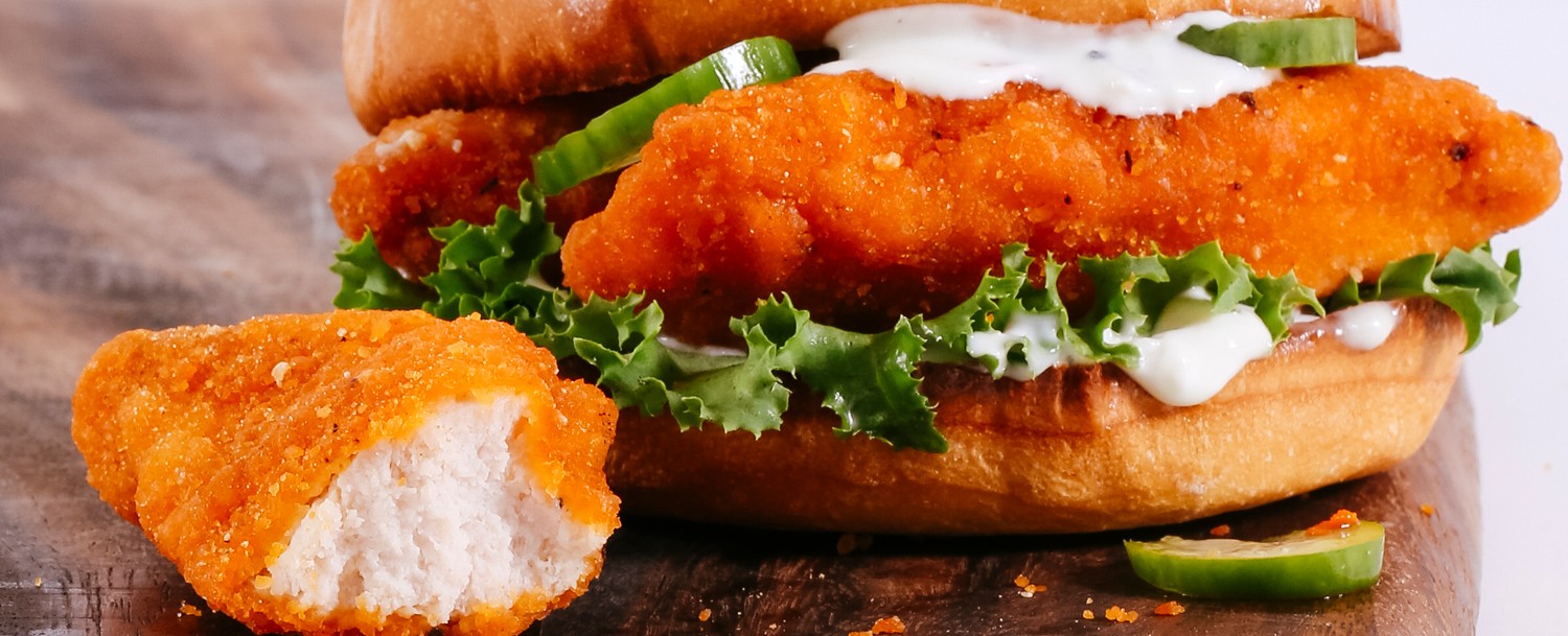 A spicy chicken tender sandwich on a wooden board 