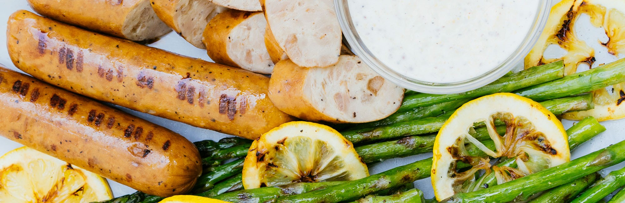 picture of dinner sausage, asparagus, and lemons on a serving platter with a side of sauce